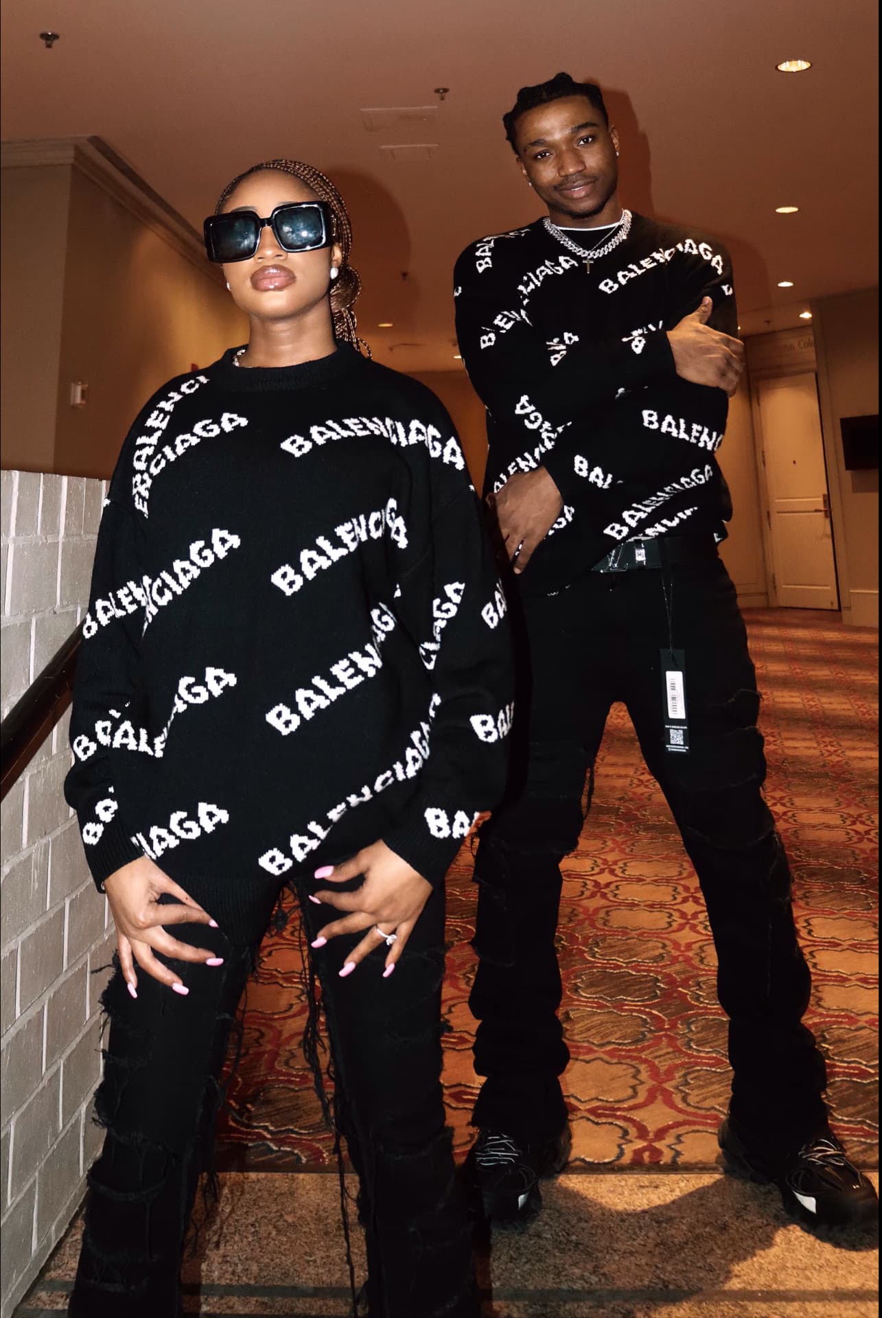 Couple in matching black designer knitwear in a hotel corridor
