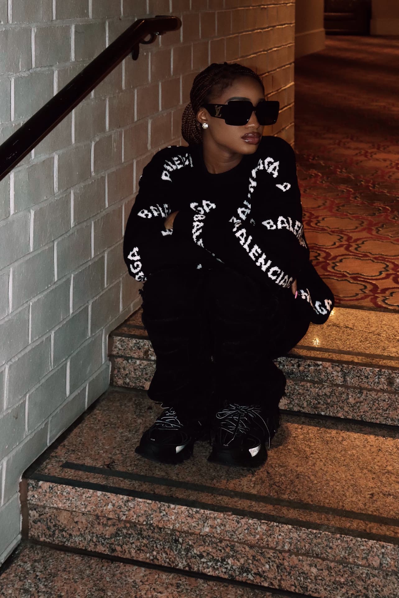 Seated stairwell portrait in all-black designer fit with sunglasses